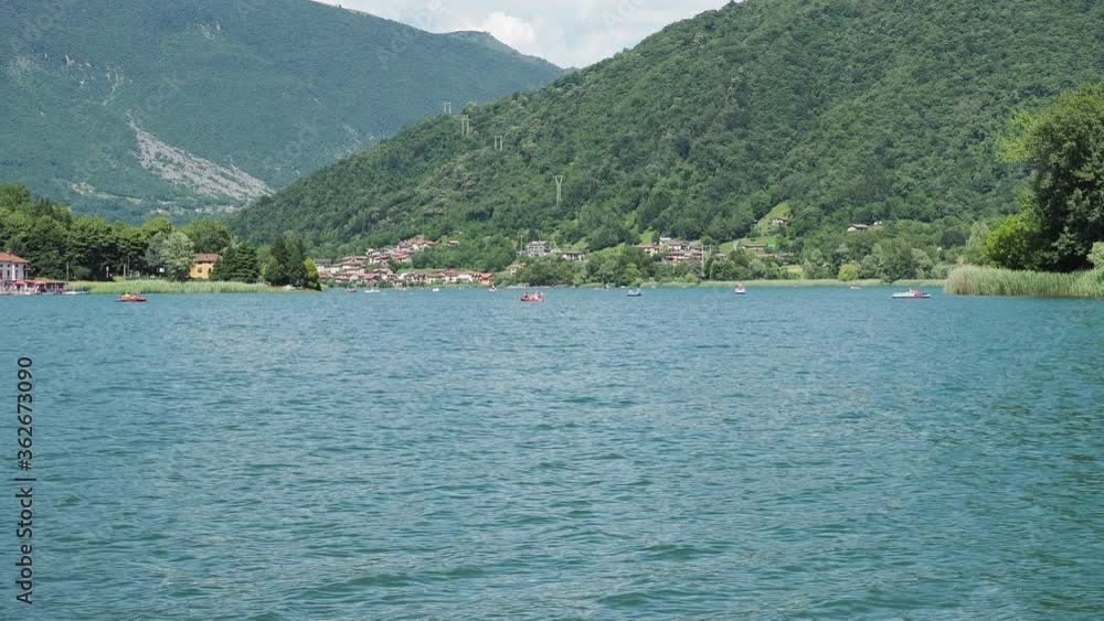 Endine lake, Bergamo, Italy. People on colorful pedal boats on the lake in summer. Touristic destination. The lake is a protected natural environment classified as a natural park Endine lake, Bergamo, Italy. People on colorful pedal boats on the lake in summer. Touristic destination. The lake is a protected natural environment classified as a natural park