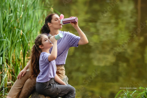 Mother and daughter on a walk in the park drinking from vacuum flask. Concept of outdoor recreation using reusable dishes. A bottle for coffee or tea to go.