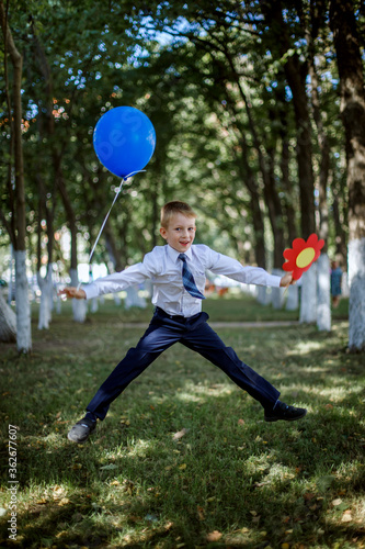 A happy boy with a balloon and a flower jumps in his school uniform