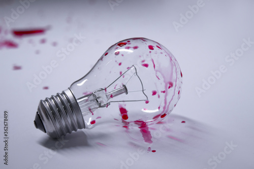 light bulb stained with red liquid - blood - on a white background in red drops. Copy space. Isolated. High quality photo