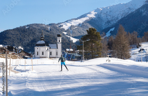 Cross-country skier on sunny track towards pitoresque church, Seefeld, Austria