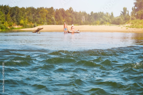 Waves on the river roll  unrecognizable travelers are walking on the water in the distance and pulling an inflatable boat. Electoral focus