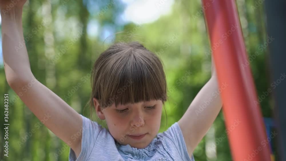 Girl performs physical exercises in the park on exercise machines. Doing sports. Physical exercise to strengthen muscles. A child performs a sports element on the crossbar. Girl performs physical exercises in the park on exercise machines. Doing sports. Physical exercise to strengthen muscles. A child performs a sports element on the crossbar.