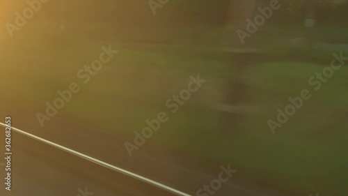 Transport, travel, road, railway, landscape, comnication concept - view from window of speed train with glare on glass and parallel rails on landscape of meadows and forest before sunset in summer photo