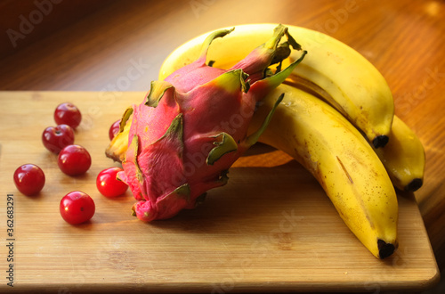 Bananas, cherries and pitaias, dragon fruit: ripe, juicy fruits lie on a wooden board on a table. photo