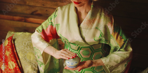 Valokuvatapetti A girl in a green kimono with red manicure holds a white and blue bowl in her ha