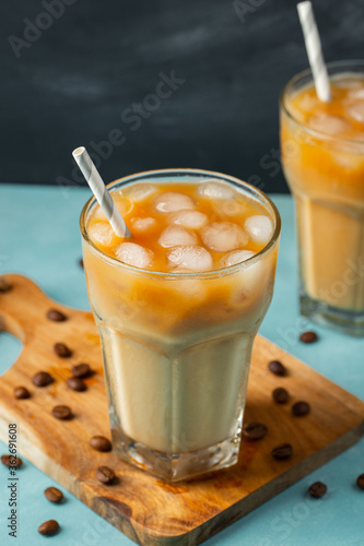 Ice coffee in a tall glass with cream poured over and coffee beans on a light stone background. Cold summer drink with tubes