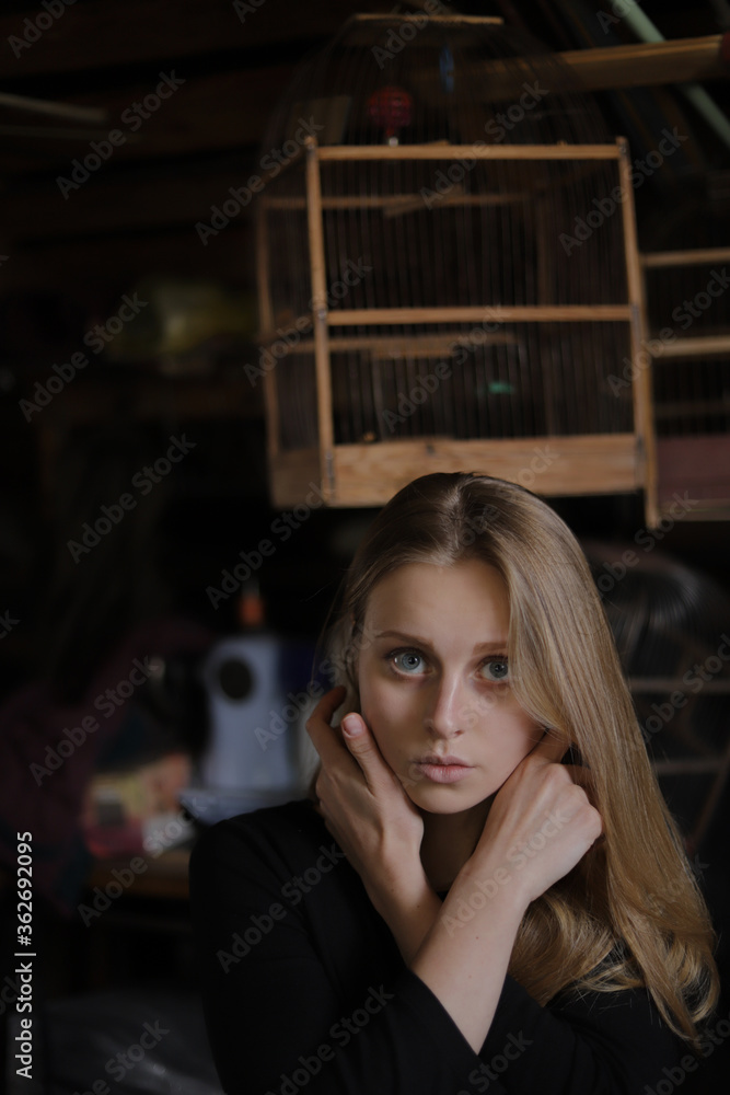 Girl blonde in black clothes in the attic, birdcage in the background, beautiful face, big eyes, dark background