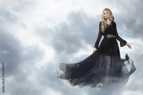 Fashion blonde in a long black dress. Background sky clouds copycpase photo