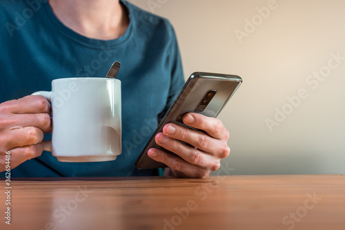 young man using his smartphone and drinking coffee inside his house