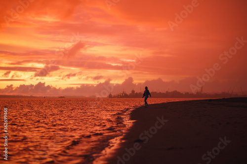 Woman walks alone on the beach at the colorful sunset after the rain. Legs in the white shoes. Red orange, crimson purple colours.