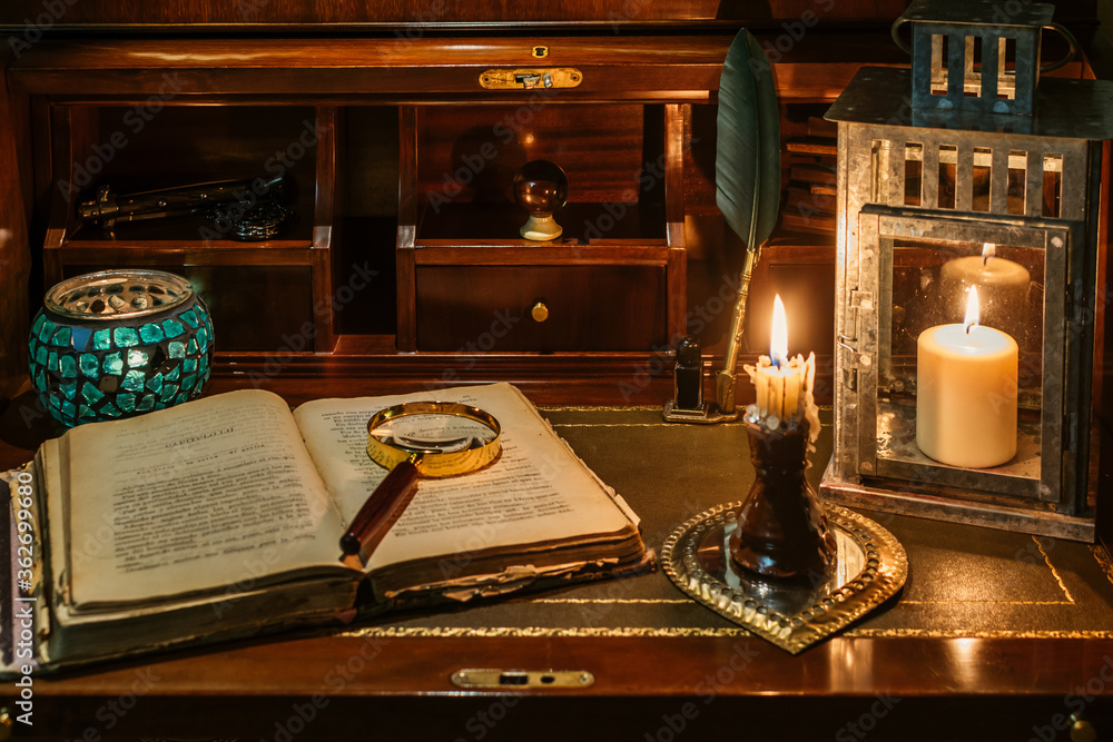 open antique book on which a magnifying glass rests. are found on a wooden desk on leather. Two lighted lanterns are incorporated to illuminate with a candle and two other writing pens open antique book on which a magnifying glass rests. are found on a wooden desk on leather. Two lighted lanterns are incorporated to illuminate with a candle and two other writing pens