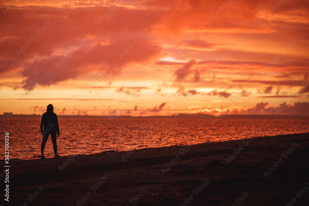 Obraz premium Woman walks alone on the beach and looks at the colorful sunset after the rain