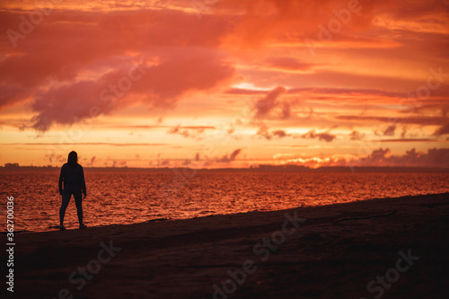 Woman walks alone on the beach and looks at the colorful sunset after the rain