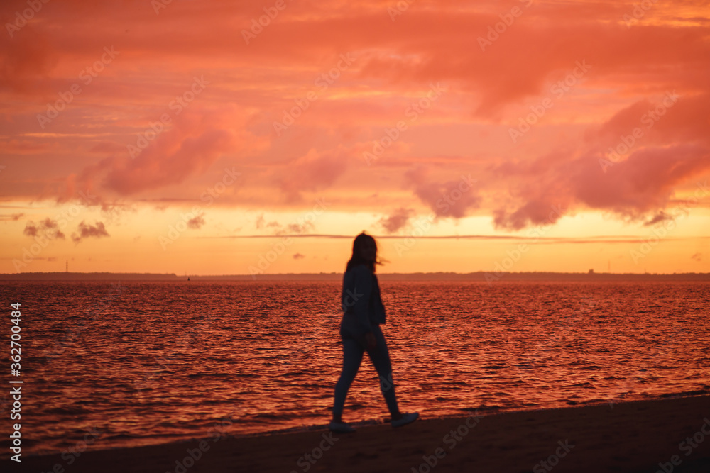 Woman walks alone on the beach and looks at the colorful sunset after the rain. Beautiful scenery, focus on waves.