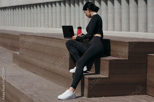 Woman athlete with the laptop resting during a morning walk before work. Brunette sitting with a computer on her lap.