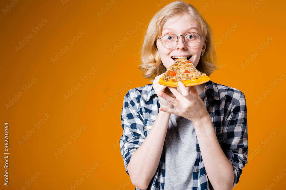 Portrait of a blonde girl in glasses who is happy to eat a slice of pizza on an orange background Portrait of a blonde girl in glasses who is happy to eat a slice of pizza on an orange background