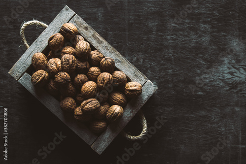 Box with tasty walnuts and nutcracker on dark wooden table, closeup
