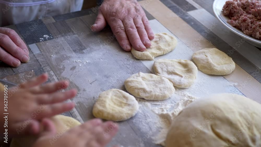 Funny blond boy helps beloved grandmother in kitchen. elderly woman rolls pastry for pasties and puts minced meat. teenager touches dough. Kid and granny are happy together. shallow depth of field Funny blond boy helps beloved grandmother in kitchen. elderly woman rolls pastry for pasties and puts minced meat. teenager touches dough. Kid and granny are happy together. shallow depth of field