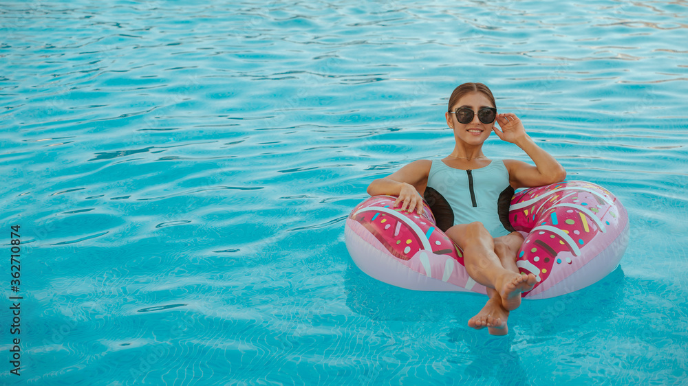 sexy girl in bikini and sunglasses swimming on inflatable donut matt in pool.