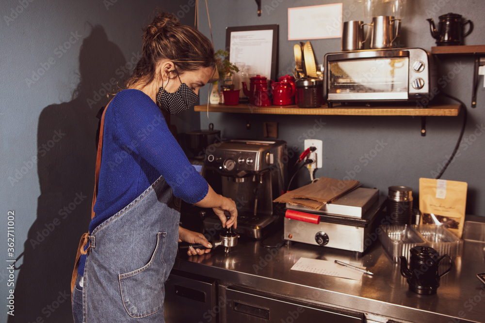 Caucasian woman making coffee in a small business wearing mask durind covid-19 pandemic reopening after quarantine Caucasian woman making coffee in a small business wearing mask durind covid-19 pandemic reopening after quarantine