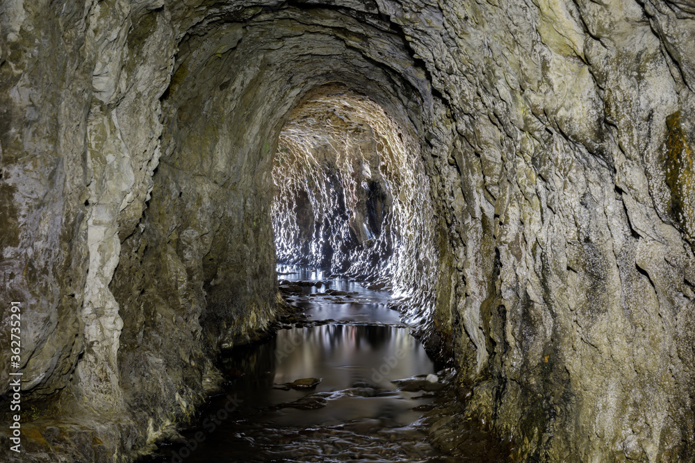 Abandoned Ocean Shore Railroad Creek Tunnel in Davenport, California, USA. Yellow Bank Creek draining through the man-made tunnel (drilled in 1907-1908) in the Santa Cruz Mudstone.

