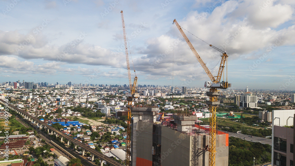 Large construction site including several cranes working on a building complex, with clear blue sky and the sun