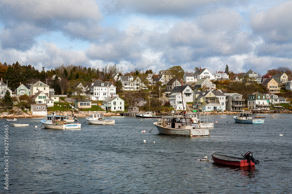 Stongington, Maine;  Lobster boats anchored in Stonington bay with New England style houses on the shore in the background.
