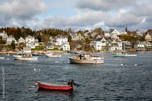 Stongington, Maine; Lobster boats anchored in Stonington bay with New England style houses on the shore in the background.