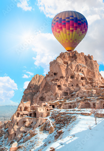 Colorful hot air balloon over the amazing rocks formations and hills in snowy winter - Cappadocia, Nevsehir
