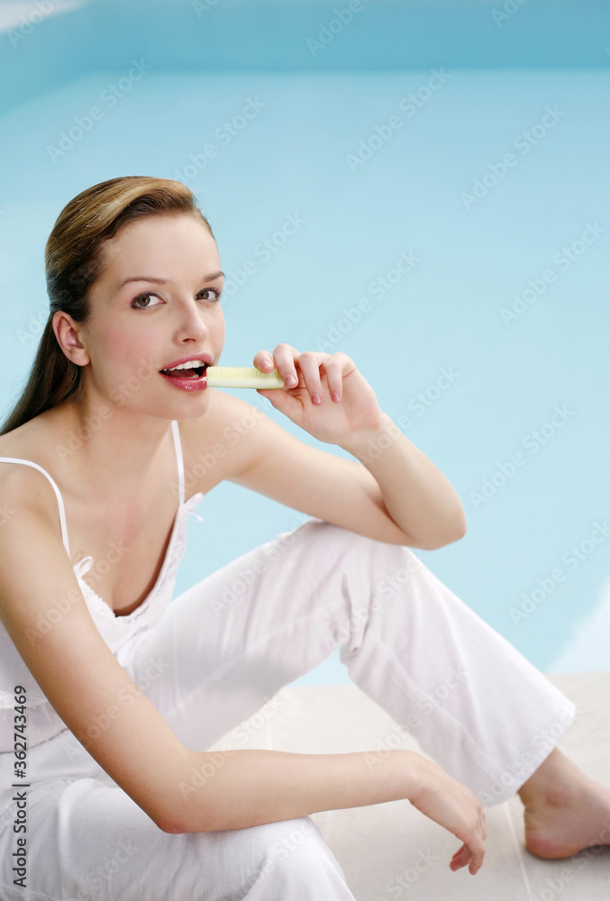 Woman sitting by the pool side eating cucumber Woman sitting by the pool side eating cucumber