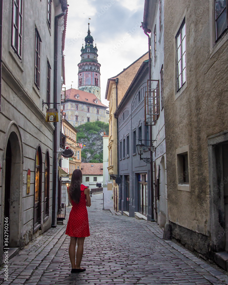 Girl in red dress watching castle from a narrow street in Cesky Krumlov, Czech Republic