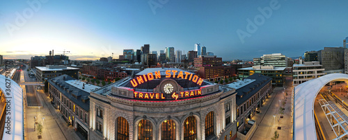 union station panorama with neon travel by train sign and clock and Denver city skyline in the background at sunrise