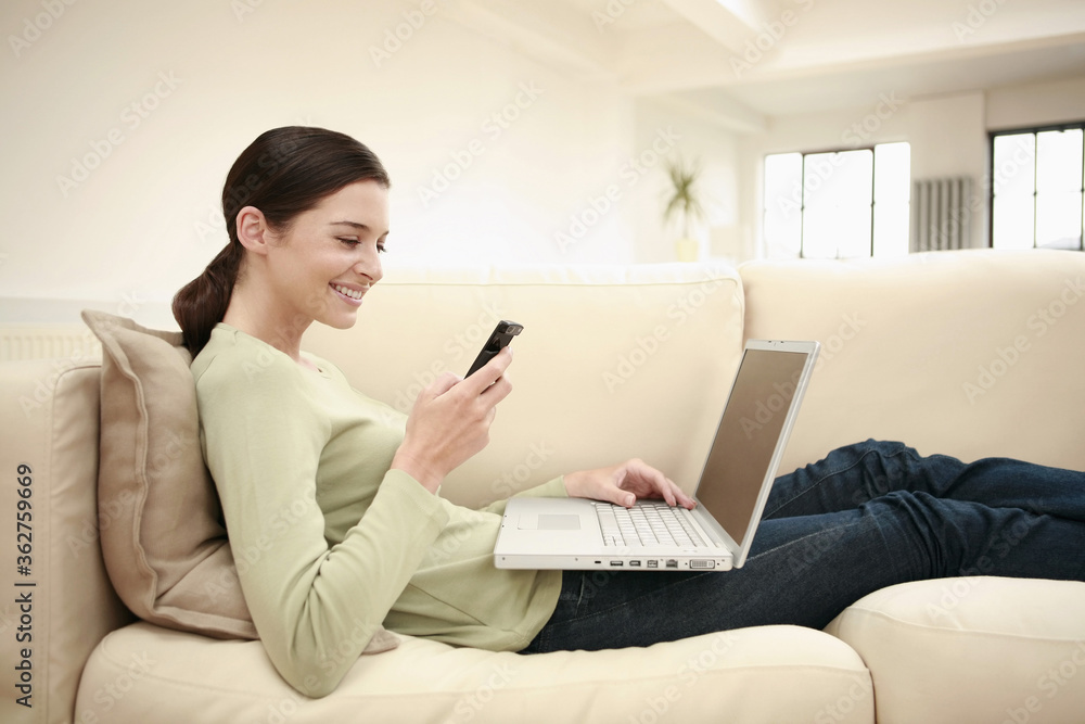 Naklejka premium Woman text messaging on the cell phone while using laptop