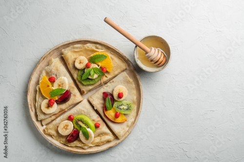 Crepes with fresh berries served with honey for breakfast over rustic table viewed from above. pancakes with fruits and honey on light background