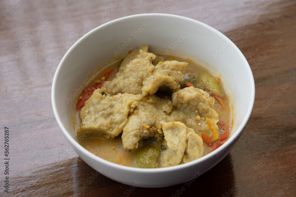 Thai food fish ball in green curry with egg plants and sweet basils in white bowl.