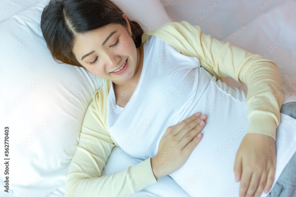 Happy pregnant young asian woman touching abdomen and admiring baby or fetus on bed with happiness smile face. Asia pregnancy mother love baby so much. Mom waiting and expecting baby has good health Happy pregnant young asian woman touching abdomen and admiring baby or fetus on bed with happiness smile face. Asia pregnancy mother love baby so much. Mom waiting and expecting baby has good health