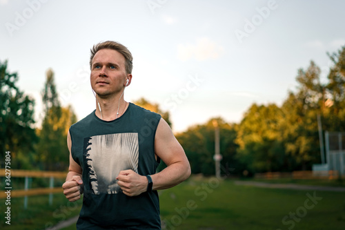 Portrait of a young man in fitness wear running in a park. Close up of a smiling man running while listening to music using earphones.