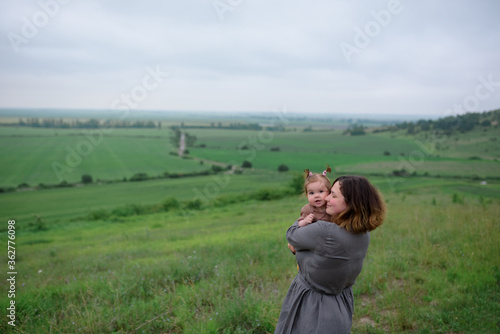 Mom holds her little daughter in her arms. Shot on a background of green hills.