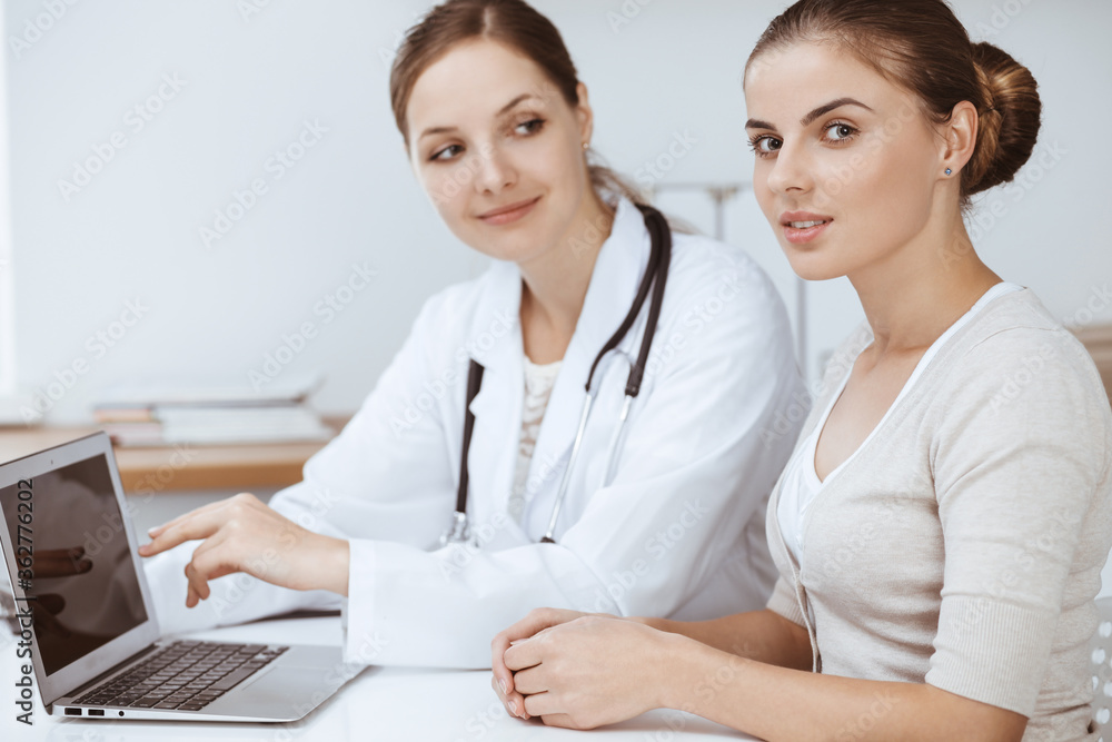 Doctor and patient are sitting and discussing health examination results while using laptop computer. Health care, medicine and good news concepts Doctor and patient are sitting and discussing health examination results while using laptop computer. Health care, medicine and good news concepts