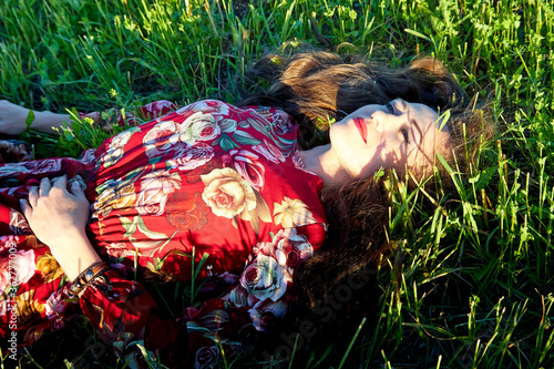 Quadro su tela Beautiful woman or girl with magnificent figure laying on the glass in green and yellow field in the setting sun during sunset with warm yellow light