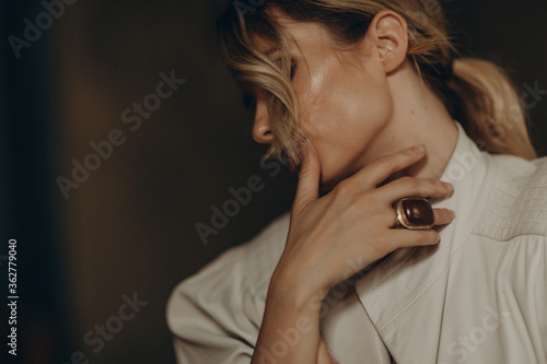portrait of a stylish blonde woman in elegant totall beige look leather trench coat, ring, and smoky eyes makeup in the studio. Spring - autumn fashion concept. Soft selective focus.