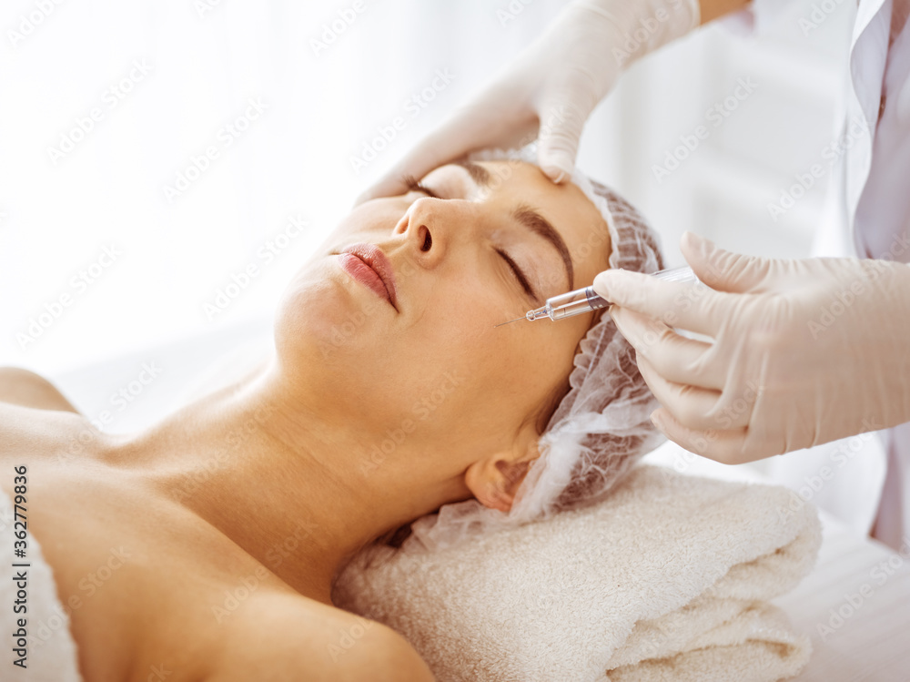 Beautician doing beauty procedure with syringe to face of young brunette woman. Cosmetic medicine and surgery, beauty injections