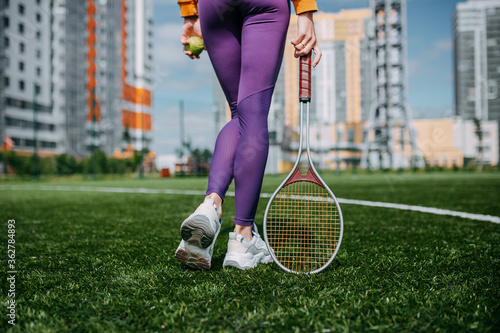 Woman playing on the tennis court. Woman holding tennis racket and ball on the green grass.