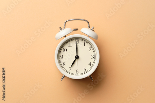White vintage alarm clock on pastel orange paper background.