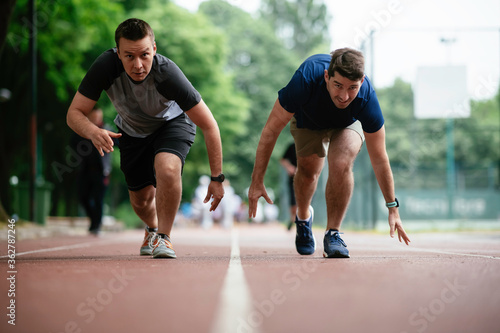Young men training on a race track. Two young friends running on the athletics track  © JustLife