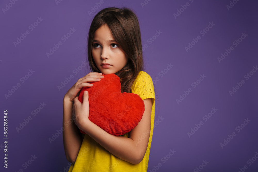 Photo of unhappy beautiful girl holding soft toy heart and looking aside Photo of unhappy beautiful girl holding soft toy heart and looking aside