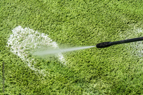 Carpet washing. Cleaning a green large hairy rug with a large jet of water photo