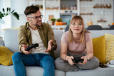Husband and wife playing video game with joysticks in living room. Loving couple are playing video games at home.	