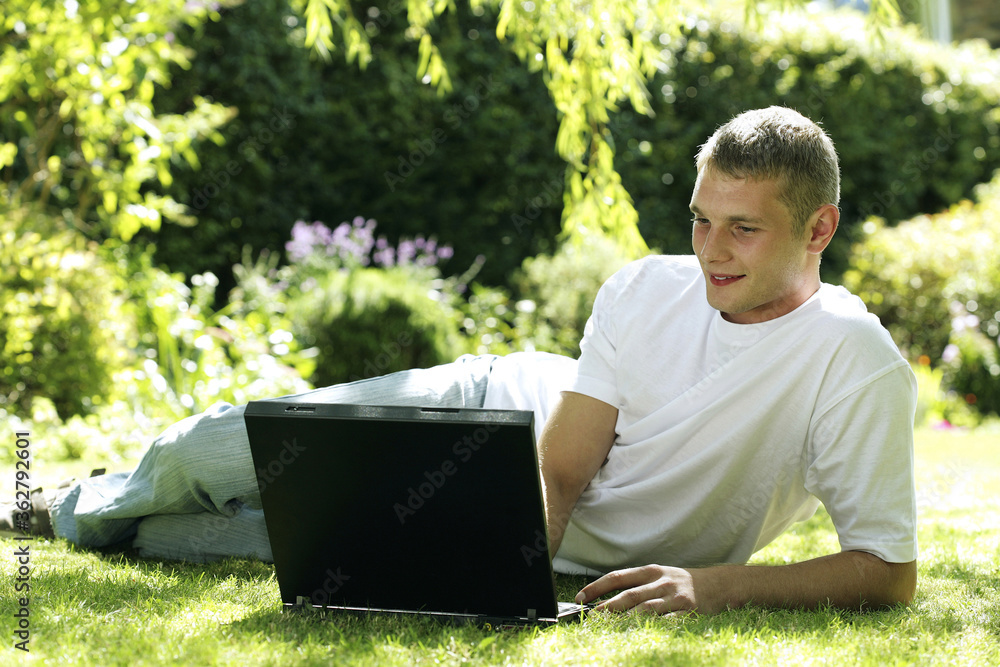 Teenage boy lying on the field using laptop
